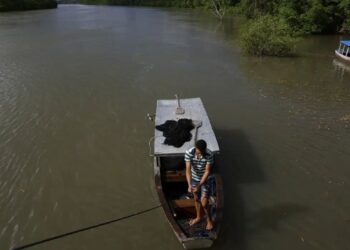 Pescador em barco no rio cercado por vegetação, símbolo da pesca artesanal.