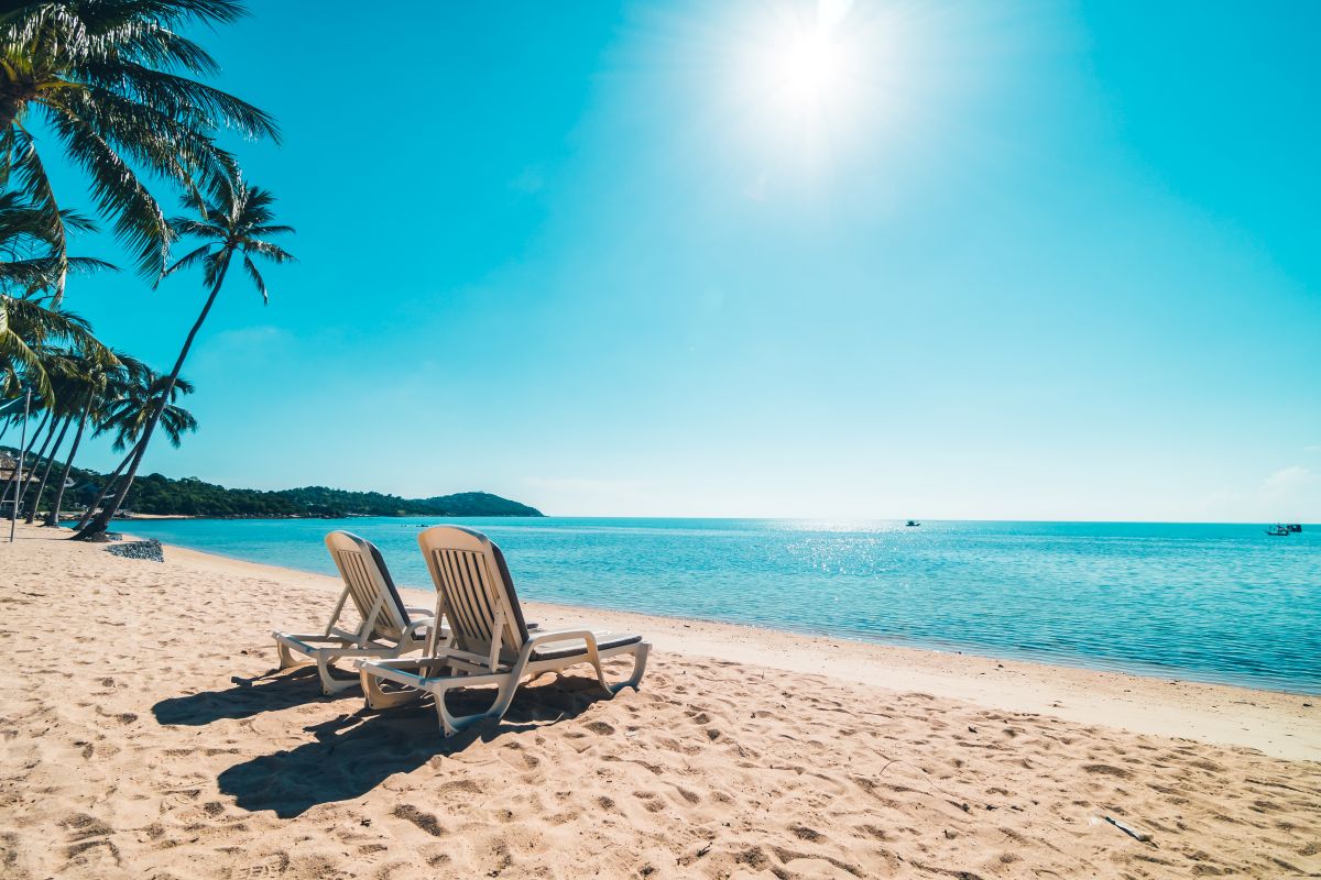 Cadeira de praia vazia em areia dourada e mar calmo, simbolizando uma viagem tranquila em setembro.