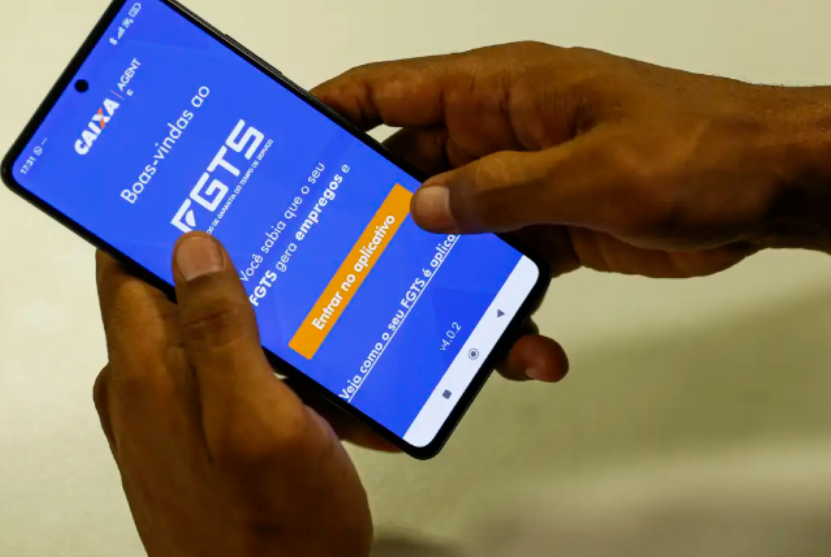 Mãos segurando celular com tela do aplicativo FGTS aberta.