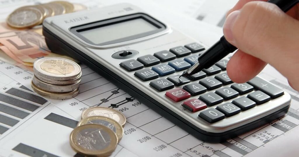 Pessoa usando uma calculadora, com moedas e gráficos financeiros ao fundo, simbolizando o planejamento financeiro pessoal.