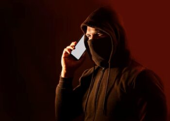 Homem encapuzado com celular, representando tentativa de golpe por telefone.
