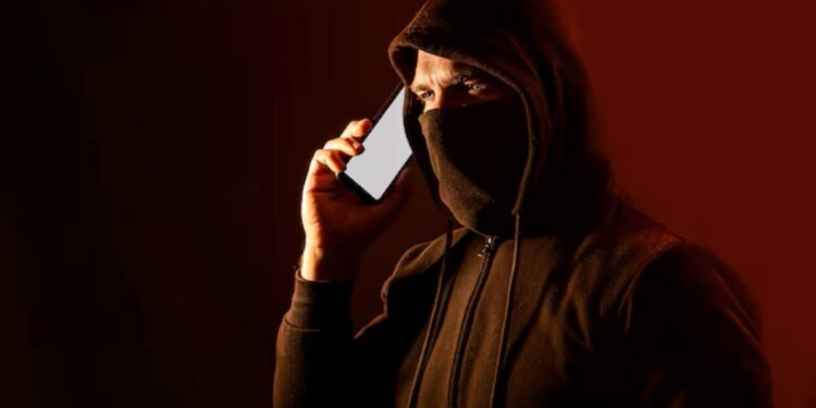Homem encapuzado com celular, representando tentativa de golpe por telefone.