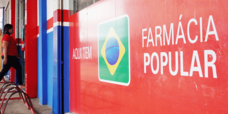 Fachada de uma farmácia com um grande cartaz vermelho e azul exibindo o logo do "Farmácia Popular" que da remédios de graça.