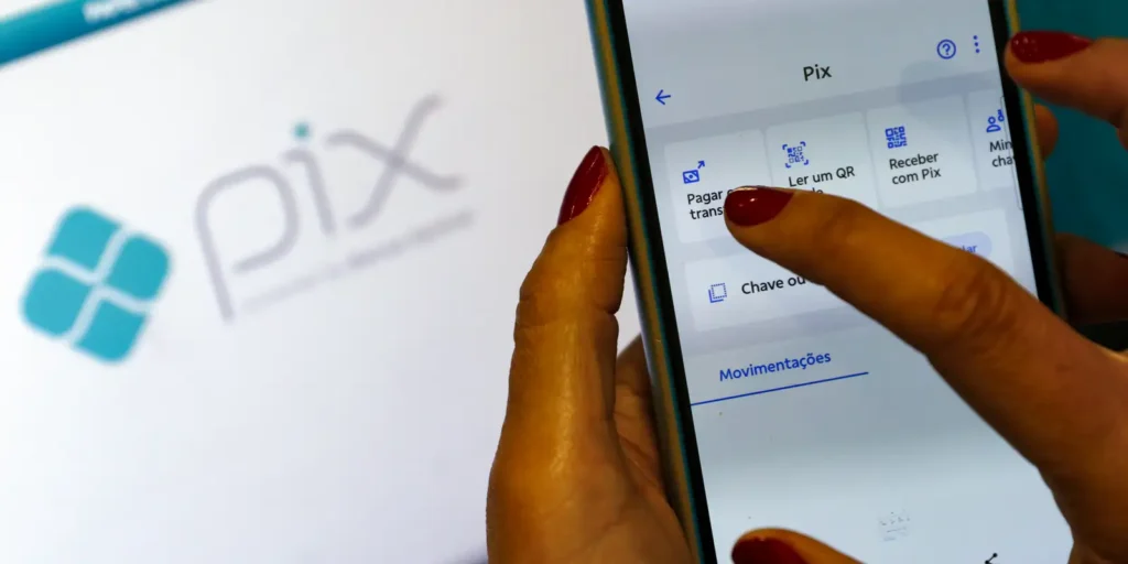 Mãos de uma pessoa usando um smartphone para fazer uma transação via Pix, com a tela do aplicativo do banco e o logo do sistema de pagamento visíveis.