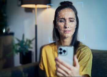 Mulher jovem tem o rosto escaneado por um smartphone, ilustrando o uso do reconhecimento facial para autenticação.