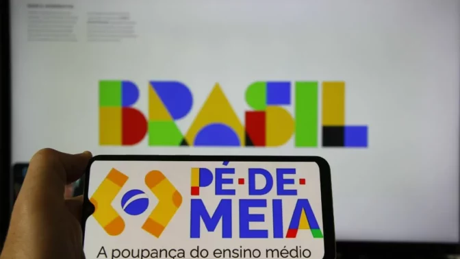 Um smartphone com a logo do programa Pé-de-Meia, com a tela do computador com a logo do governo Brasil ao fundo.