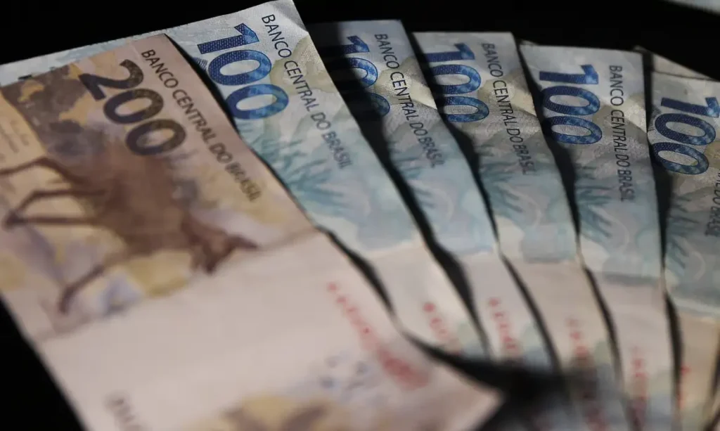 Várias notas de R$ 100 e R$ 200 espalhadas sobre uma mesa, simbolizando o impacto financeiro da proposta de ajuste do piso salarial nacional para R$ 1.631 em 2026.
