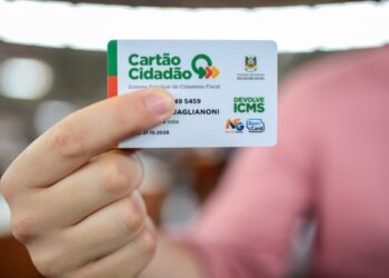 Mão segurando o Cartão Cidadão do programa Devolve ICMS, mostrando detalhes como o logotipo do Rio Grande do Sul e a validade.