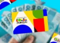 Cartão colorido do programa Bolsa Família segurado sobre cédulas de dinheiro em fundo azul