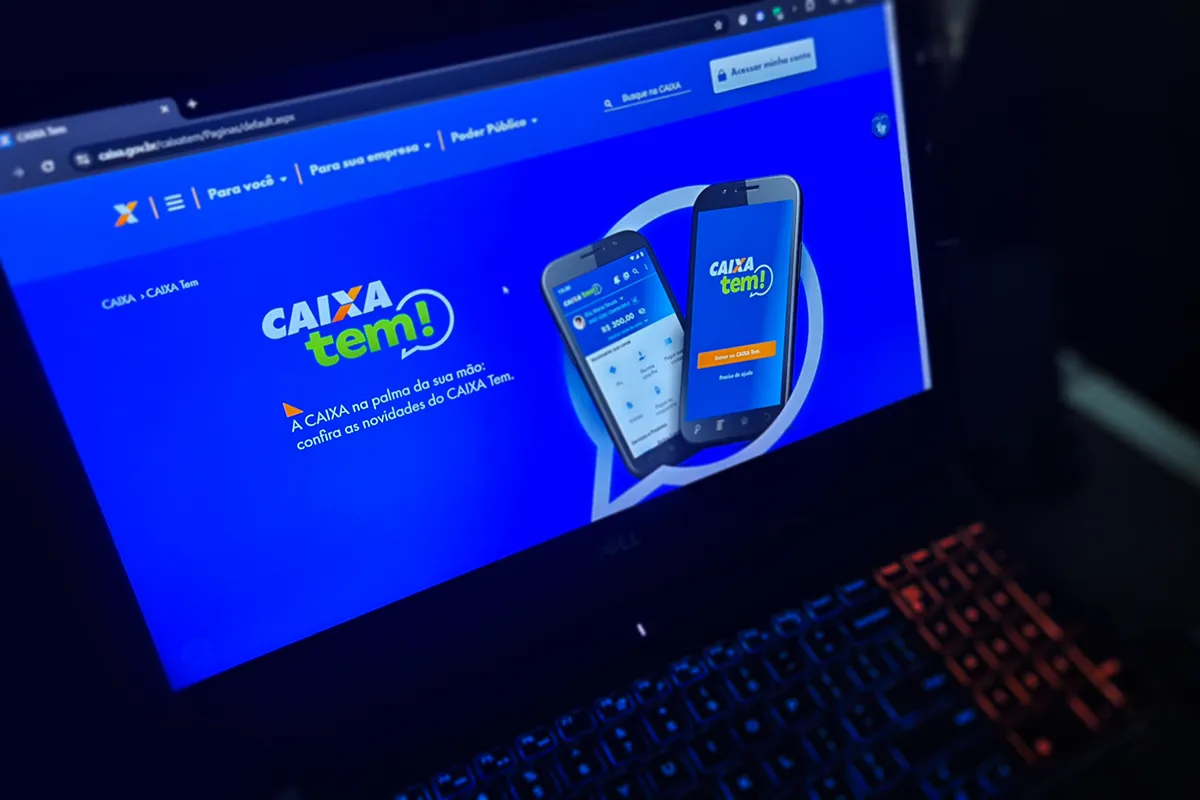 Página principal do aplicativo Caixa Tem exibida em tela de notebook com fundo azul e dois celulares ilustrando a interface do app.