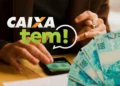 Pessoa usando o aplicativo Caixa Tem em um smartphone, com notas de R$ 100 espalhadas e o logo 'CAIXA tem!', indicando a liberação de valores.