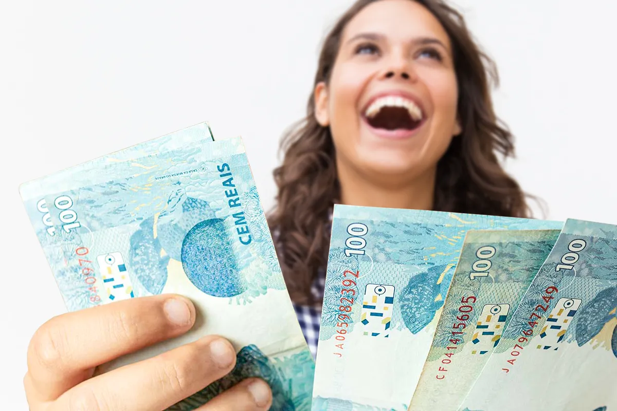 Mulher jovem comemora segurando notas de R$ 100, representando o recebimento de benefícios ou pagamentos.