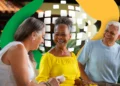 Grupo de idosos sorrindo e conversando em ambiente ao ar livre com decoração colorida ao fundo