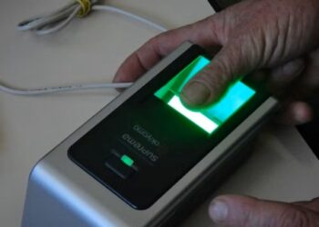 Um dedo sendo posicionado em um leitor biométrico com luz verde, representando a nova exigência de cadastramento para o BPC/Loas.