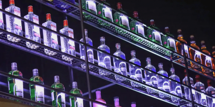 Várias garrafas de bebida alcoólica organizadas em prateleiras iluminadas com luzes coloridas