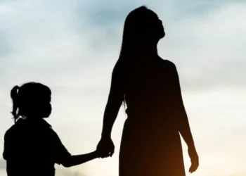 Silhueta de mulher e criança pequena de mãos dadas com céu ao fundo no pôr do sol