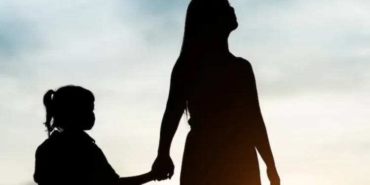 Silhueta de mulher e criança pequena de mãos dadas com céu ao fundo no pôr do sol