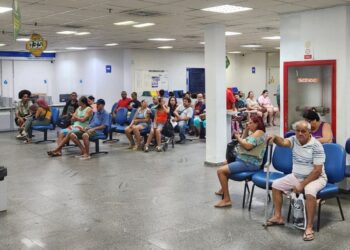 Pessoas em uma sala de espera, sentadas em cadeiras azuis, aguardando atendimento durante um mutirão extraordinário do INSS.