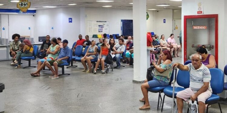 Pessoas em uma sala de espera, sentadas em cadeiras azuis, aguardando atendimento durante um mutirão extraordinário do INSS.