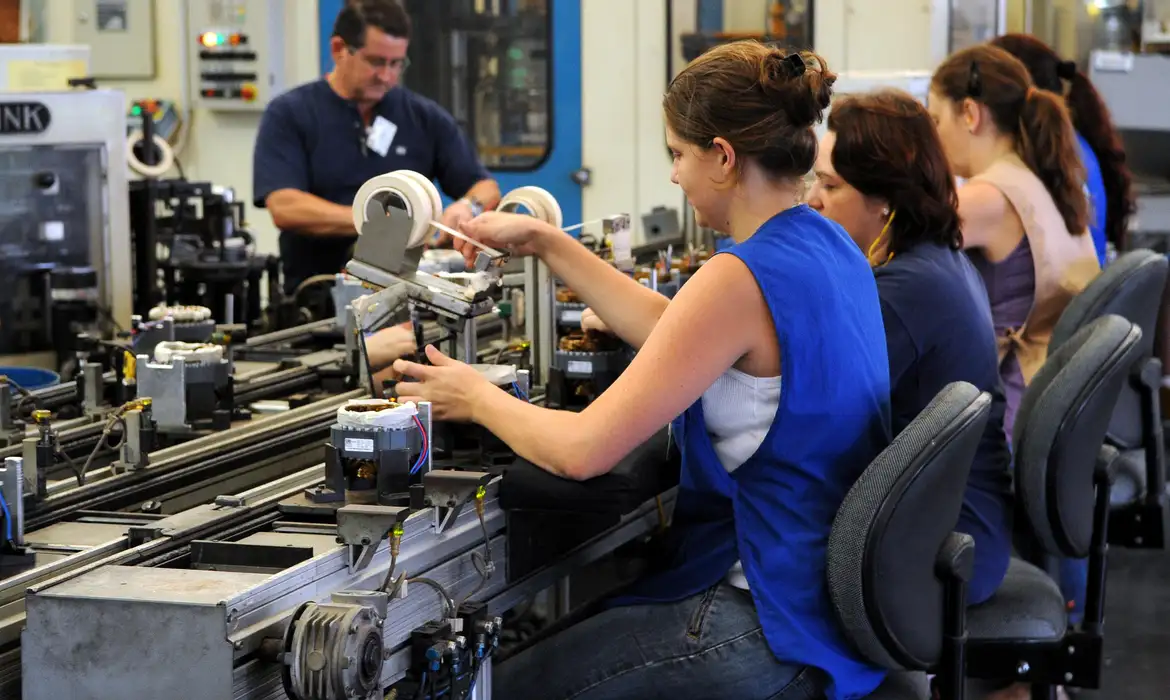 Pessoas trabalhando em linha de produção com máquinas industriais em fábrica moderna