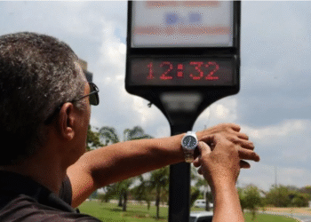 Homem ajusta o relógio de pulso observando painel digital de hora em via pública durante o anúncio sobre o horário de verão.