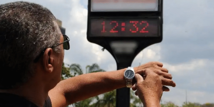 Homem ajusta o relógio de pulso observando painel digital de hora em via pública durante o anúncio sobre o horário de verão.