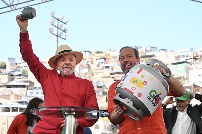 Lula lança programa Gas do Povo no Rio de Janeiro. Lula com chapéu levantando panela e homem segurando botijão do programa Gás do Povo em favela do Rio.