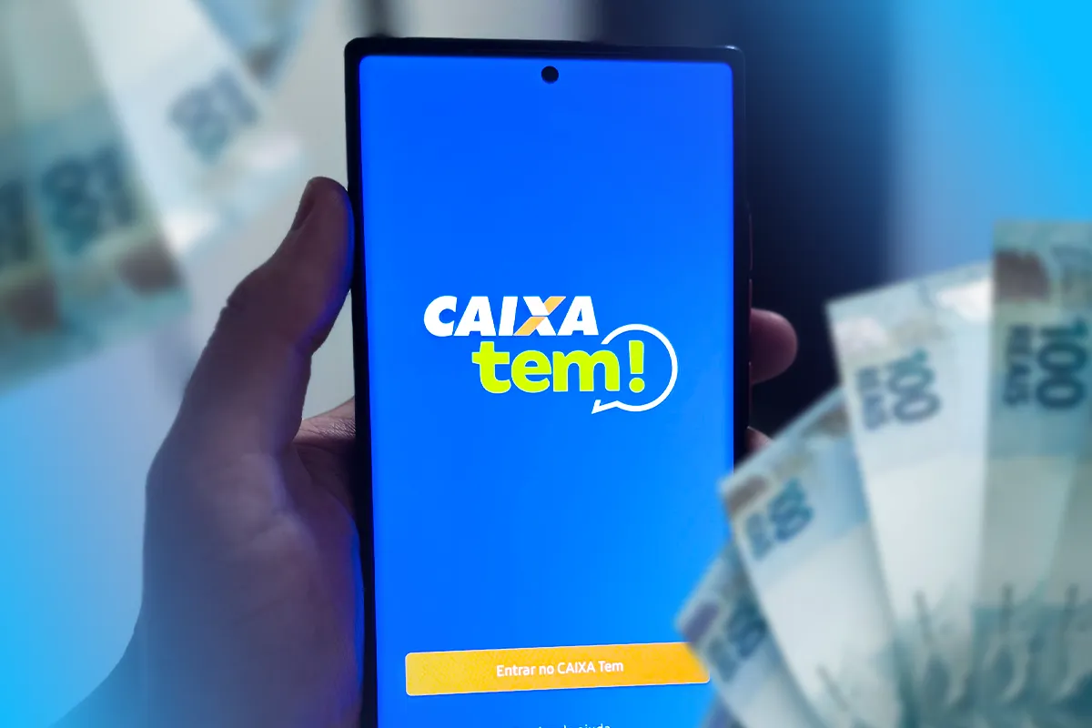 Mão segurando celular com aplicativo CAIXA Tem aberto e cédulas de 100 reais ao fundo desfocado