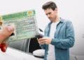 Um homem branco segura seu celular ao lado de um carro enquanto outro detalhe mostra a nova Carteira Nacional de Habilitação (CNH) brasileira em primeiro plano.