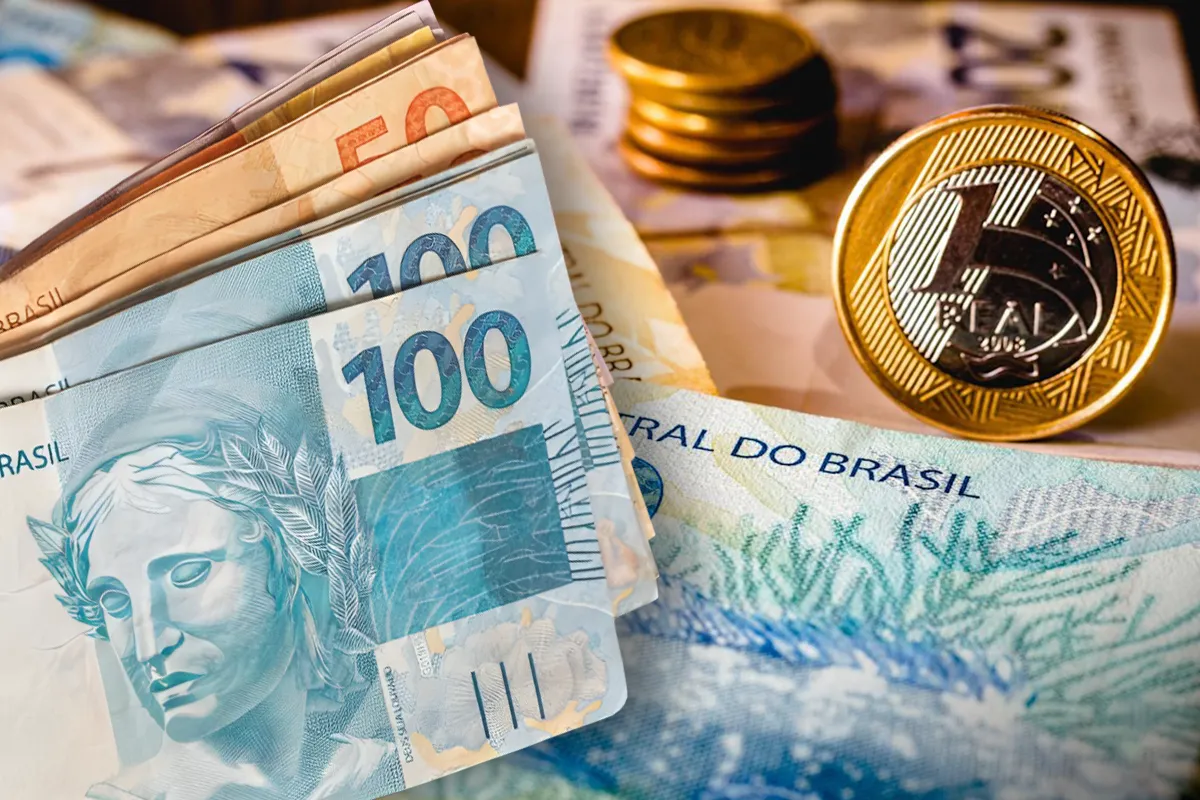 Dinheiro em cédulas de 50 e 100 reais junto a moedas de real em fundo desfocado