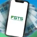 Smartphone com logotipo do FGTS na tela e várias notas de 100 reais ao fundo