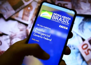 Smartphone exibindo app oficial do Auxílio Emergencial do Governo Federal em fundo de cédulas de reais