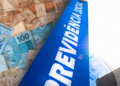 Cédulas de dinheiro (reais) em destaque, simbolizando o pagamento da Previdência Social, com a palavra "PREVIDÊNCIA SOCIAL" sobreposta em letras grandes azuis.