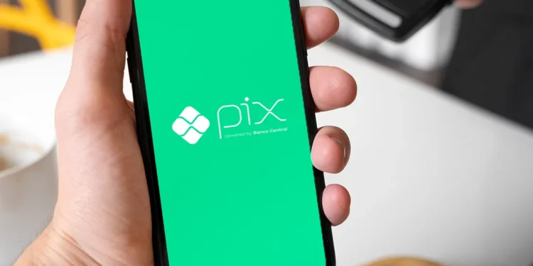 Mão segurando smartphone com tela verde exibindo o logo do PIX do Banco Central