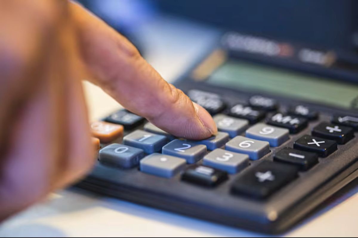 Imagem de uma mão digitando números em uma calculadora, representando cálculos para o Imposto de Renda.