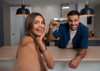 Casal feliz em casa nova, o homem exibindo chaves, representando a conquista de um imóvel com descontos.