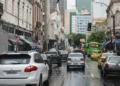 Rua movimentada com vários carros e ônibus em dia chuvoso no centro de uma grande cidade