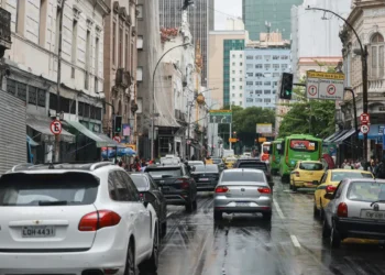 Rua movimentada com vários carros e ônibus em dia chuvoso no centro de uma grande cidade