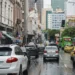 Rua movimentada com vários carros e ônibus em dia chuvoso no centro de uma grande cidade