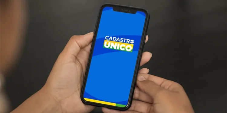 Pessoa segurando celular com aplicativo Cadastro Único aberto em tela azul.