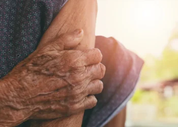 Mãos enrugadas de pessoa idosa apoiando seu próprio braço à luz do sol