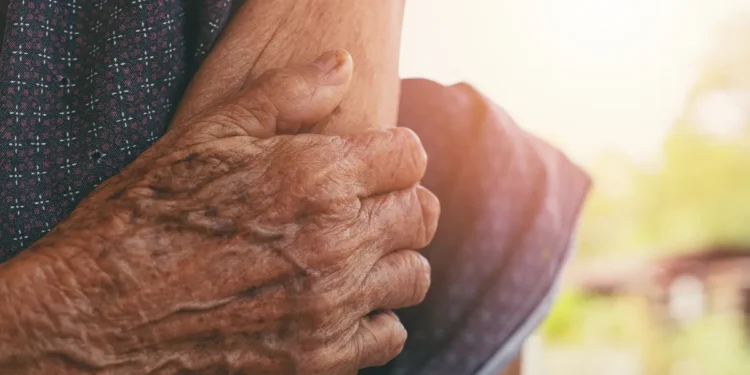 Mãos enrugadas de pessoa idosa apoiando seu próprio braço à luz do sol