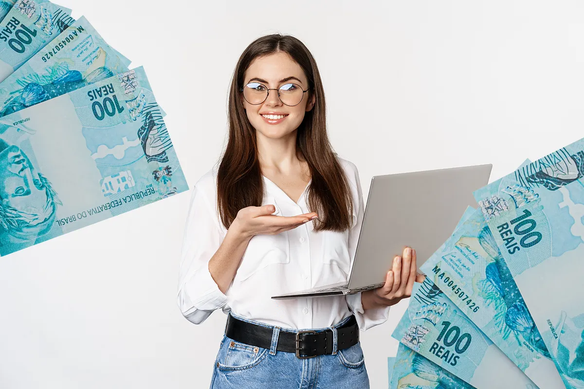 Dicas para ganhar dinheiro online em 2026 Jovem sorrindo com notebook nas mãos, com notas de 100 reais ao redor