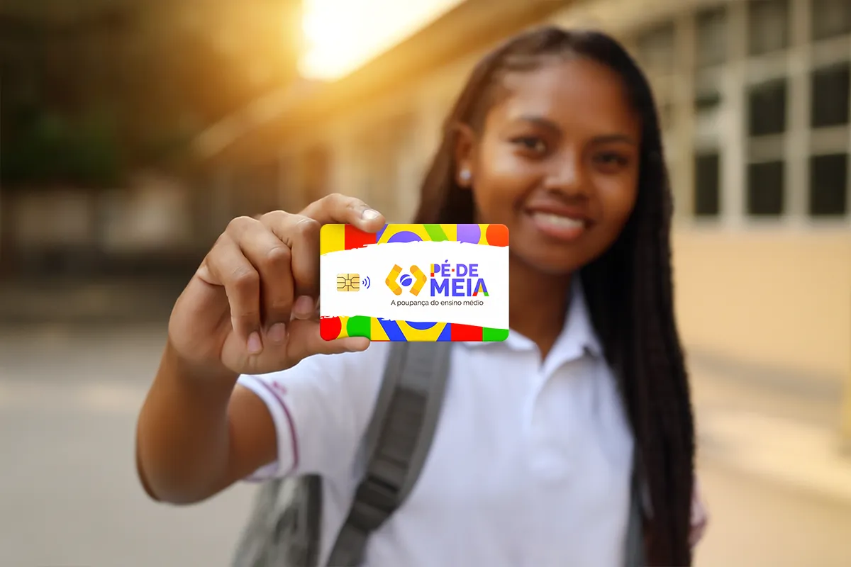 Jovem exibe cartão Pé-de-Meia do Ensino Médio em 2026. Estudante sorrindo segura cartão do programa Pé-de-Meia, destaque colorido.