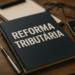 Caderno com o texto reforma tributária de 2026 ao lado de calculadora, dinheiro e óculos.