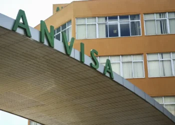 Detalhe da fachada da Anvisa com letras verdes grandes sobre estrutura cinza em prédio com janelas