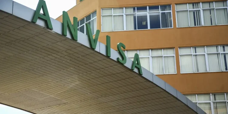 Detalhe da fachada da Anvisa com letras verdes grandes sobre estrutura cinza em prédio com janelas