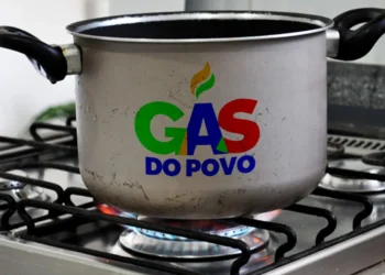 Panela no fogão com chama acesa e o logo do programa Gás do Povo estampado.