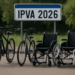 Duas bicicletas e duas cadeiras de rodas com placa IPVA 2026 ao fundo em área externa.