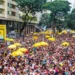 Multidão animada com guarda-chuvas amarelos durante o Carnaval de São Paulo.